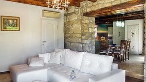 A modern living room with a white leather sofa, a chandelier, stone walls, and a wooden ceiling. - Charming 2BR Villa with pool for 4+1, for small groups, pet-friendly (Buzet)