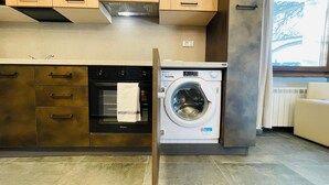 A modern kitchen with a built-in oven, a washing machine, and a window with curtains. - Villa Linda - ONE-BEDROOM APARTMENT sleeps 5 (Bardonecchia)