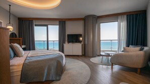 Une chambre d’hôtel moderne équipée d’un lit, d’une télévision, d’un coin salon et offrant une vue sur la mer.