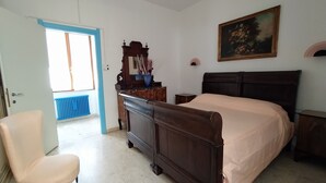 A bedroom with a bed, a chair, a dresser, a mirror, and a painting on the wall.