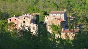 Un ensemble de bâtiments en pierre aux toits recouverts de tuiles rouges, entouré d’une forêt verdoyante et dense.