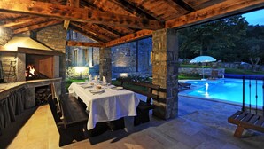 Un espace extérieur aménagé pour les repas, avec une cheminée en pierre, une piscine et un bâtiment en pierre en arrière-plan.