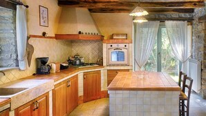 Une cuisine rustique avec des meubles en bois, un dosseret carrelé, un four encastré et un grand îlot central doté d’un évier.