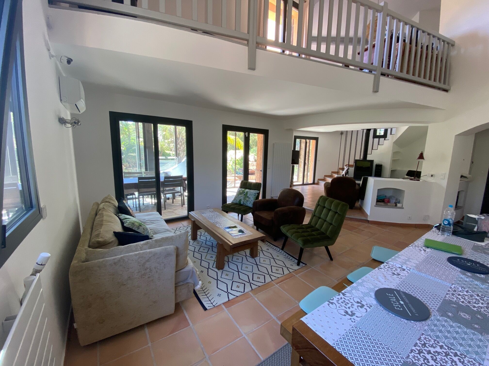 A spacious living area with a sofa, armchairs, a coffee table, and a dining table. There are large sliding glass doors leading to an outdoor patio.