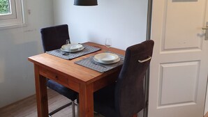 A dining area with a wooden table, two chairs, a wall clock, and a door with a hanging sign. - Family friendly chalet in the Veluwe, Gelderland, Wolfheze (Wolfheze)
