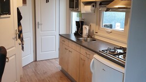 A compact kitchen with wooden cabinets, a built-in microwave, a gas stove, and a small refrigerator. - Family friendly chalet in the Veluwe, Gelderland, Wolfheze (Wolfheze)