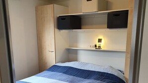A bedroom with a bed, a nightstand, a shelf with storage baskets, and a ceiling light. - Family friendly chalet in the Veluwe, Gelderland, Wolfheze (Wolfheze)