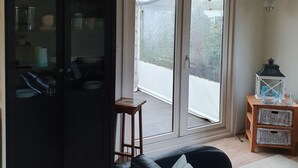 A living room with a black leather sofa, a wooden side table with a lantern, and a sliding glass door leading to a balcony. - Family friendly chalet in the Veluwe, Gelderland, Wolfheze (Wolfheze)