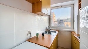 Cozinha compacta com azulejos brancos, bancada de madeira e janela com vista para a cidade.