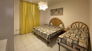 A bedroom with two beds, a yellow curtain, a ceiling light, and a painting on the wall. - Maristella, a few steps from the center and the beach (Marina di Campo)