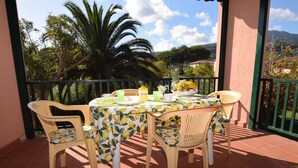 A balcony with a table set for two, surrounded by chairs, with a view of palm trees and a mountain in the background. - Maristella, a few steps from the center and the beach (Marina di Campo)