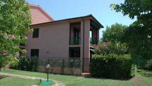 A two-story brick building with a balcony, surrounded by greenery and a fenced yard. - Maristella, a few steps from the center and the beach (Marina di Campo)
