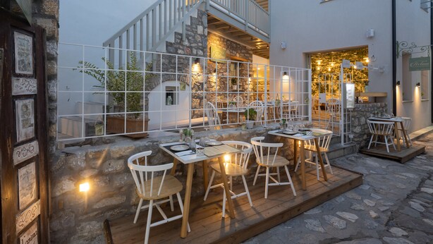 A restaurant with outdoor seating, stone walls, and a staircase leading to an upper level. - L'anima suites (Skiathos)
