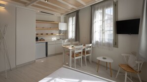 A modern hotel room with a bed, a small dining table with chairs, a kitchenette, and a TV mounted on the wall. - L'anima suites (Skiathos)