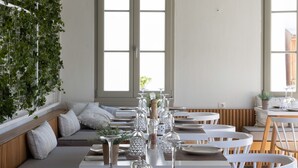 A restaurant with a modern interior, featuring white furniture, green plants on the ceiling, and large windows. - L'anima suites (Skiathos)