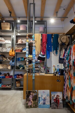 A boutique store with shelves of handbags and accessories, wooden beams on the ceiling, and a display of hats and scarves. - L'anima suites (Skiathos)