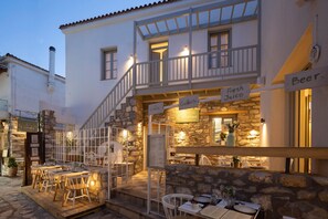 A restaurant with outdoor seating, stone walls, and a sign indicating it serves coffee, cocktails, and fresh juice. - L'anima suites (Skiathos)