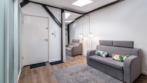 Un salon moderne avec un canapé gris, un plafond bordé de noir et un grand miroir qui reflète la pièce.
