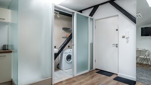 Une cuisine moderne équipée d’un lave-linge intégré, d’une porte blanche et d’un petit coin salon avec une chaise et une table.