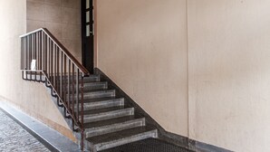 Un escalier avec une rampe en métal menant à une porte, un paillasson noir au bas de l’escalier et un chemin pavé le long du bâtiment.