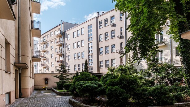 Une cour pavée avec un bâtiment doté de balcons et d’un arbre.