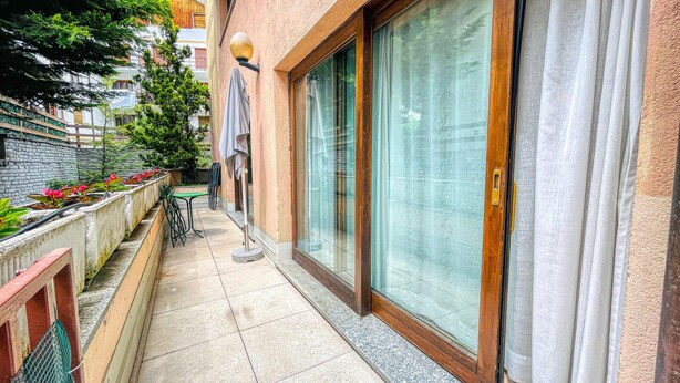 A narrow outdoor corridor with a tiled floor, a small table, and chairs, leading to a sliding glass door. - Villa Frejus - CLASSIC ONE-BEDROOM APARTMENT sleeps 5 (Bardonecchia)
