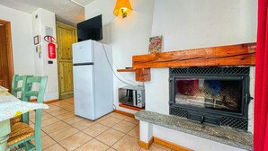 A compact kitchen with a white refrigerator, a built-in oven, a wooden mantel above a black stove, and a dining area with a table and chairs. - Villa Frejus - CLASSIC ONE-BEDROOM APARTMENT sleeps 5 (Bardonecchia)