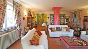 A cozy living room with two white sofas, a red armchair, and a coffee table. There is a bookshelf filled with books and decorative items. - Villa Perla by VILLASRETREATS w/Pool, A/C, WiFi, BBQ near 5 Terre (Pignone (La Spezia))