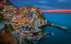A coastal town with colorful buildings perched on a cliff, a rocky shoreline, and boats docked at a pier. - Villa Perla by VILLASRETREATS with a pool, air conditioning, Wi-Fi, and a barbecue area near the Cinque Terre (Pignone (La Spezia))