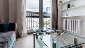 A modern room with a glass table, a sofa, a radiator, and a view of a cityscape through a window. - Chlodna 15 Apartment (Warsaw)
