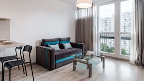 A modern living room with a sofa, two chairs, a glass coffee table, and large windows with curtains. - Chlodna 15 Apartment (Warsaw)