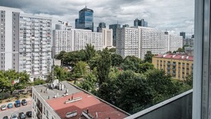 A high-rise building with multiple floors, a parking lot with several cars, and a red-roofed building in the foreground. - Chlodna 15 Apartment (Warsaw)