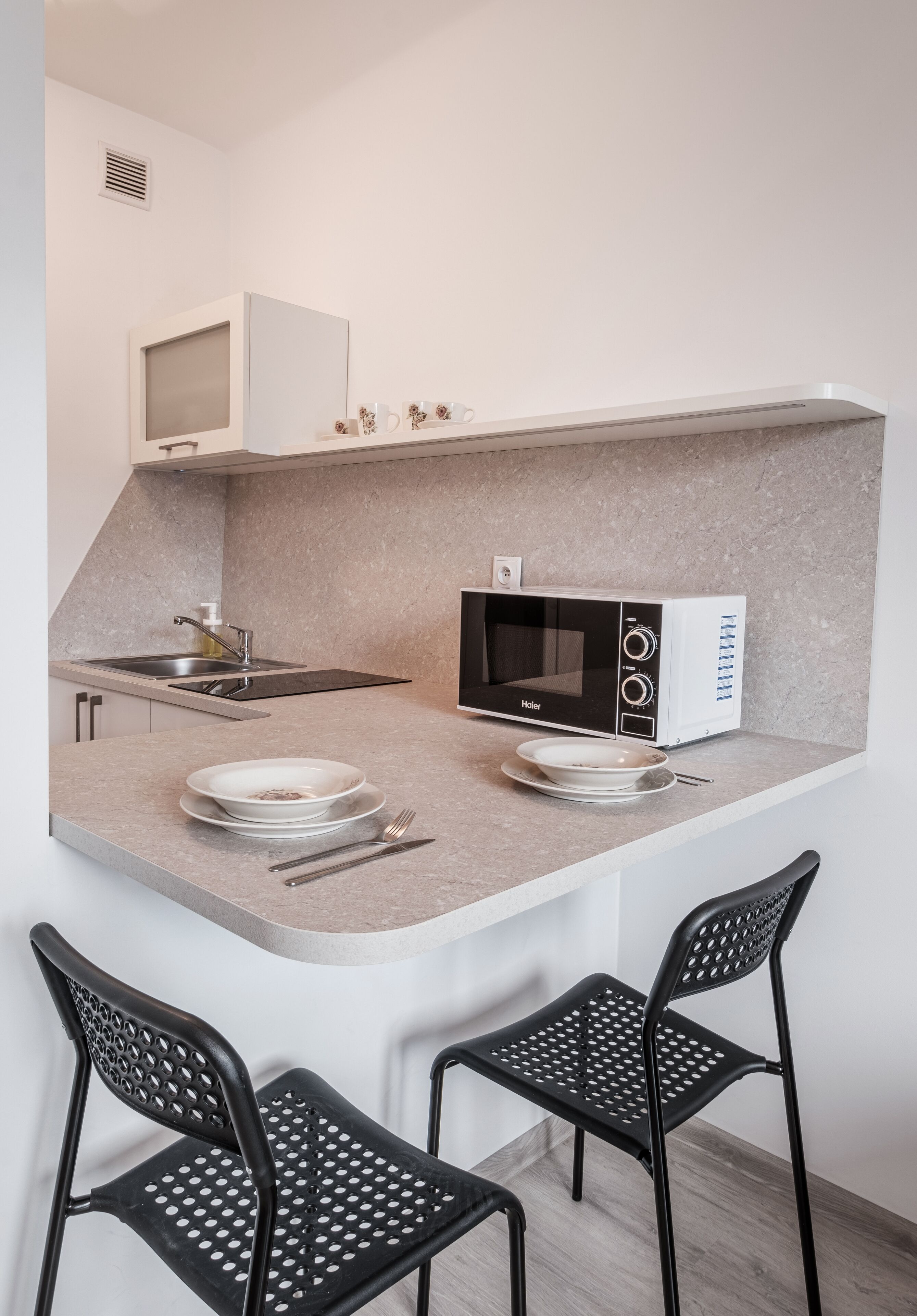 A compact kitchen with a microwave, a sink, and two chairs.