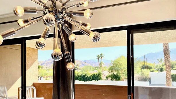 A modern room with a ceiling light fixture, a sliding glass door leading to an outdoor area with a view of mountains and greenery. - Mod Downtown Escape, Pool, Spa, Tennis, Pickleball (Palm Springs)