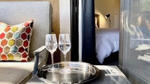 A hotel room with a bed, a sofa, a colorful pillow, a tray with two glasses, and a door leading to another room. - Mod Downtown Escape, Pool, Spa, Tennis, Pickleball (Palm Springs)