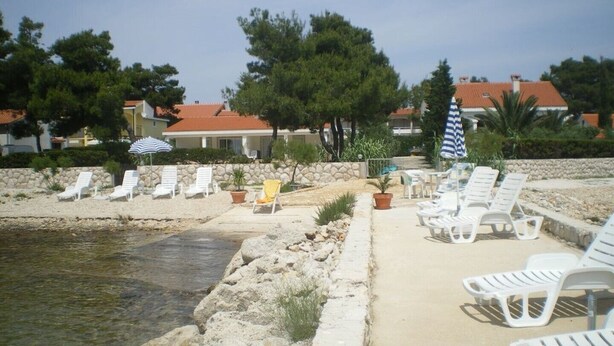Ein Strandbereich mit weißen Liegestühlen, einem kleinen Pool und einer Steinmauer.