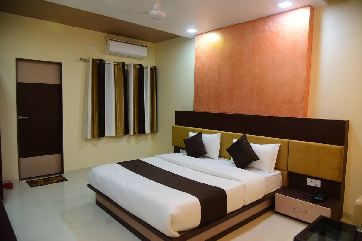 A hotel room with a bed, a nightstand, a drawer, a glass table, and a wall-mounted air conditioner.