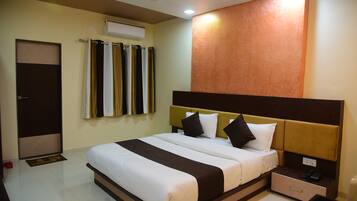 Habitación de hotel con cama, mesita de noche, cajón, una mesita de vidrio y aire acondicionado de pared.