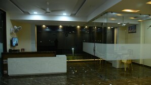 Uma área de recepção com piso de mármore, balcão de atendimento, divisória de vidro e ventilador de teto.