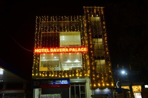Un bâtiment sur lequel on peut lire l’inscription « HÔTEL SAVERA PALACE » et où l’on aperçoit une enseigne indiquant la présence d’une agence de la banque DENA BANK.