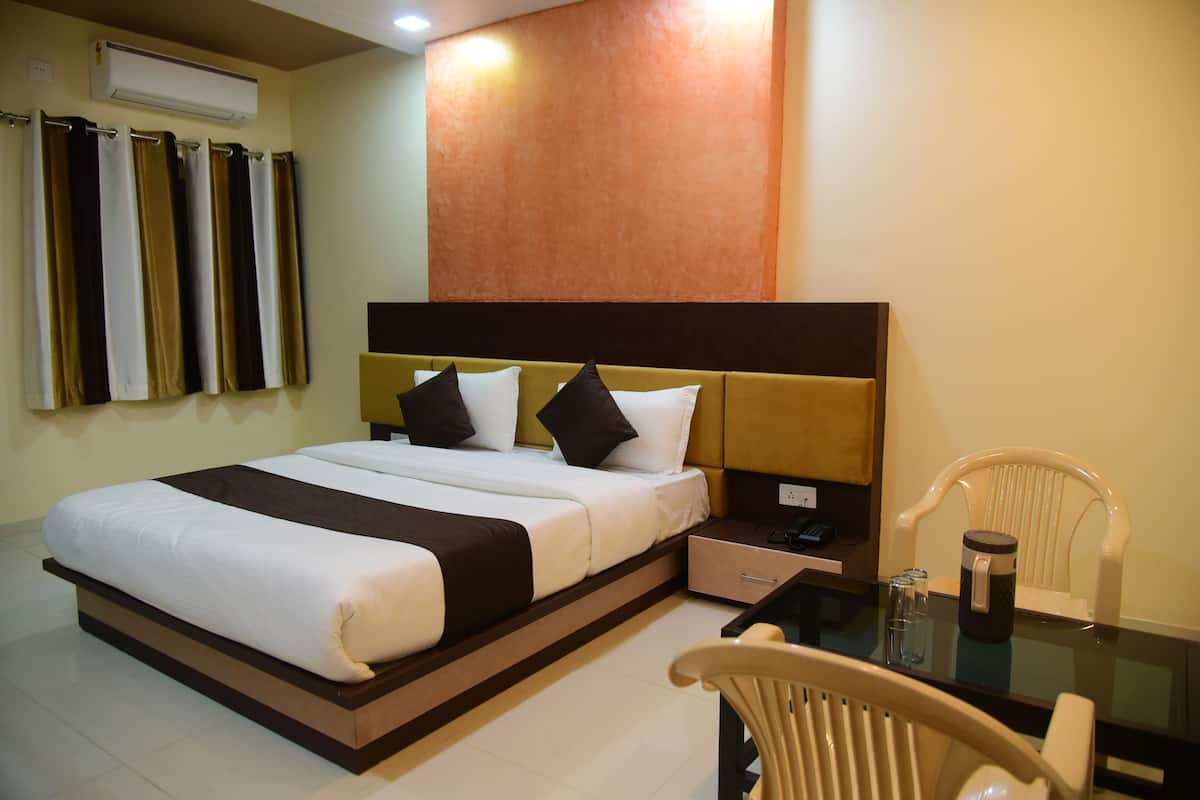A hotel room with a bed, bedside table, chair, and a wall-mounted air conditioner.