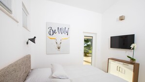 A bedroom with a bed, a wall-mounted TV, a bedside table with a plant, and a door leading to a balcony.