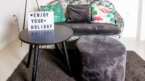 A modern living room with a sofa, a small round table, a sign that reads "ENJOY YOUR HOLIDAY", and a floor lamp.