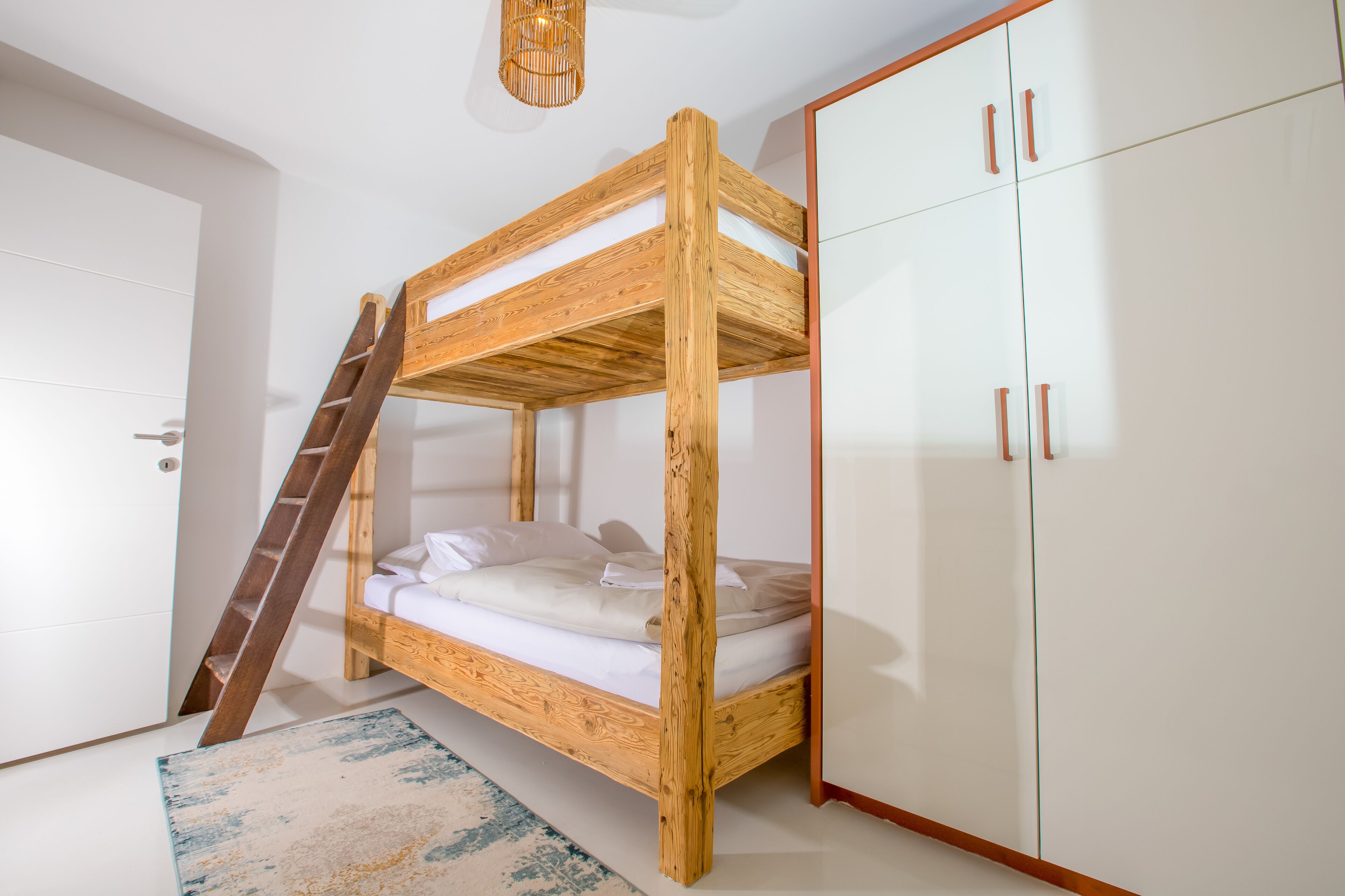 Een stapelbed met houten frame, een witte deur en een garderobe met glazen deuren.