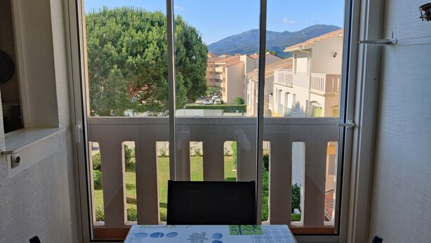 A balcony with a table and chairs, overlooking a residential area with houses and a mountain in the background. - Air-conditioned apartment. Close to shops and sea. Parking. Rated Atout France 1*. (Argelès-sur-Mer)