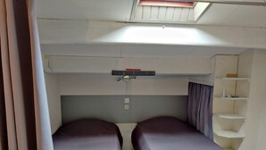 A compact room with two beds, a skylight, a small shelf unit, and a curtain. - Air-conditioned apartment. Close to shops and sea. Parking. Rated Atout France 1*. (Argelès-sur-Mer)
