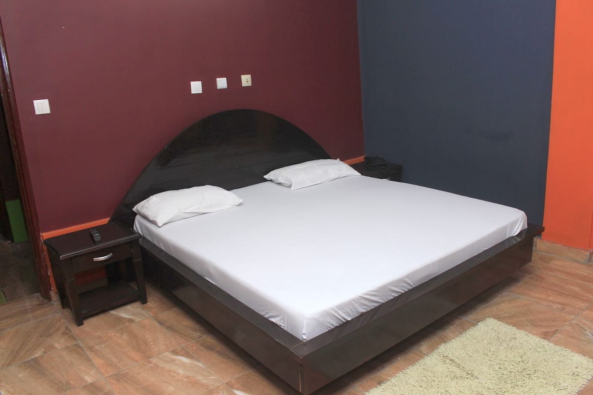 A single bed with a dark headboard, white bedding, and a small bedside table with a remote control.