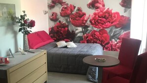 A bedroom with a bed, a dresser, a chair, and a wall with a floral mural. - Chambre d'Hôte Pivoine (Fralignes)