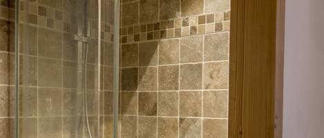 A glass-enclosed shower with a tiled wall and wooden framing.