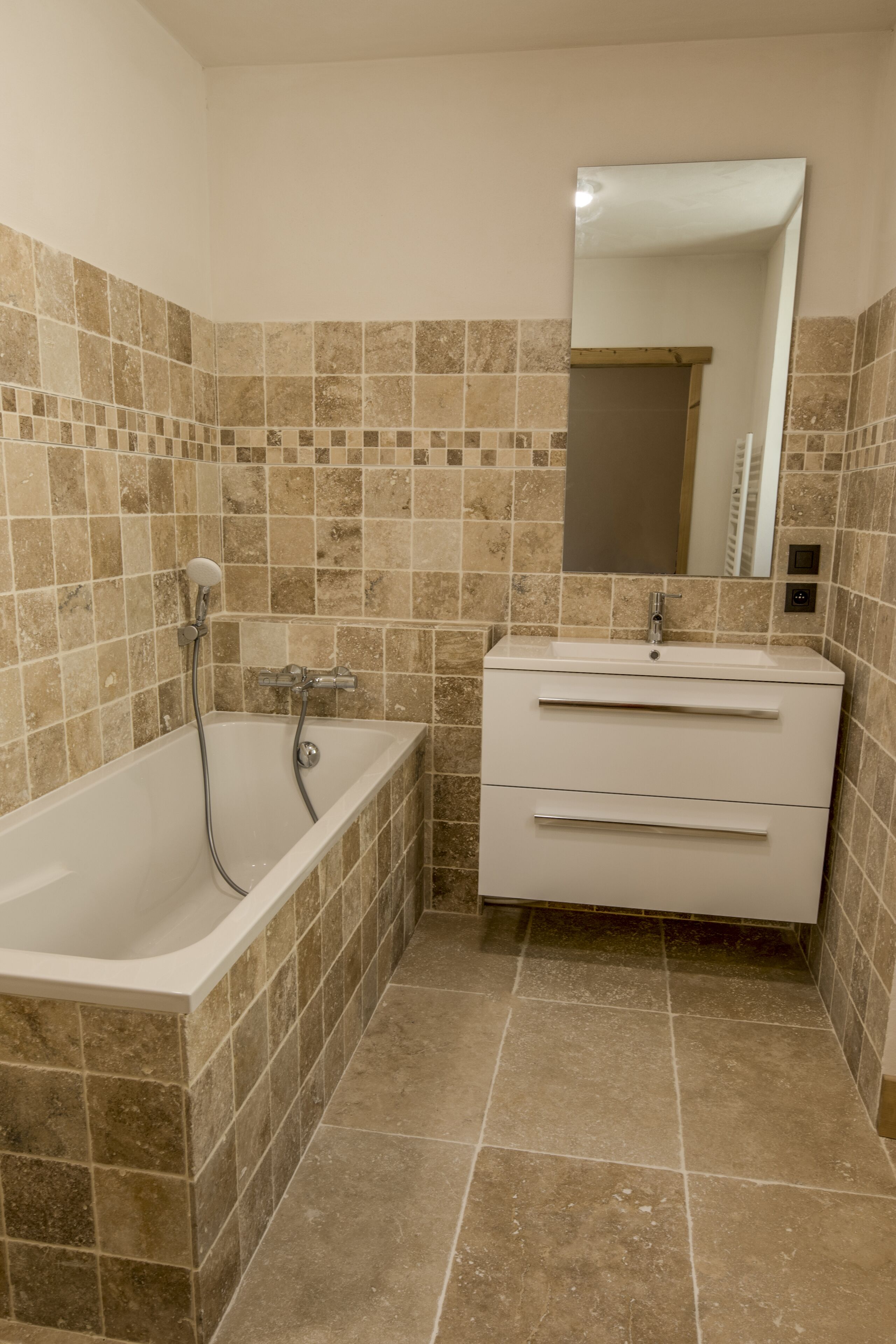 Une salle de bain avec une baignoire, un meuble-lavabo avec un miroir, et des murs et un sol carrelés.